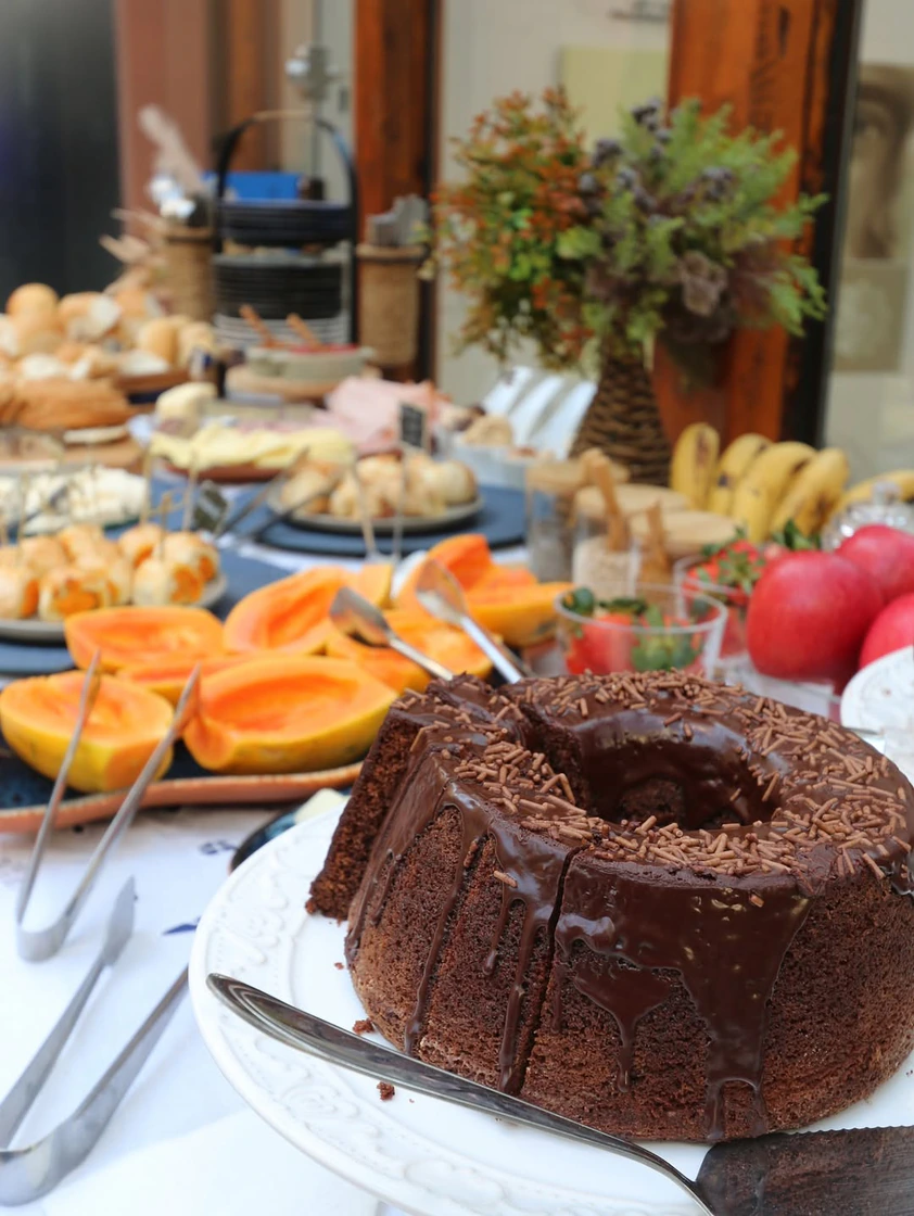 Mesa de coffee break com frutas, pães e bolo de chocolate no The Roof 448